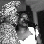 Photograph of Pamela Hart singing with a woman